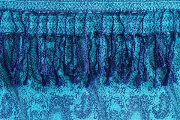 Woolen, cashmere patterned shawl or turquoise scarf with tassels. Blue background.