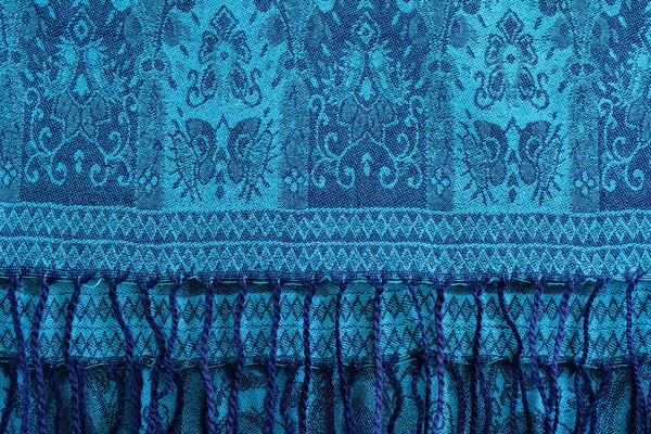 Woolen, cashmere patterned shawl or turquoise scarf with tassels. Blue background.