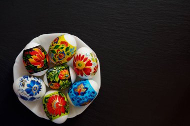 Koyu arka plan üzerinde plaka çiçek desenli parlak çok renkli Paskalya yumurtaları. Dini tatil sembolü.