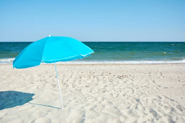 Turquoise beach umbrella by sea shore. Sunny hot day on the sandy beach.