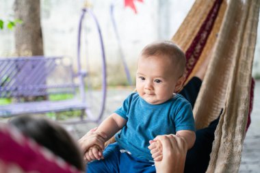 Küçük çocuk ve annesi hamakta oturuyorlar, ikisi de mutlu.