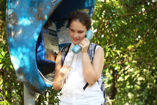 the girl is talking on the phone from the phone booth in the open air