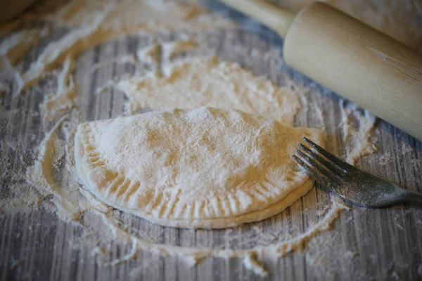 Homemade chebureks are cooked on the table with flour