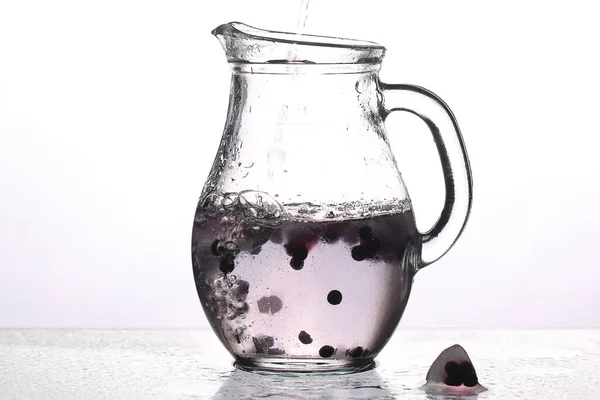 carafe of water ice and blueberries on a white background