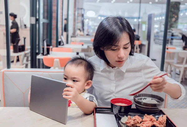 La madre asiática está comiendo en un restaurante. Mientras su hijo se sentaba watchi —  Fotos de Stock