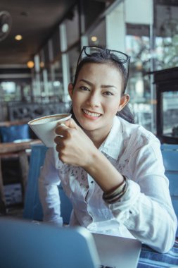 Gülümseyen mutlu Asyalı kadın kahve içerken oturuyor