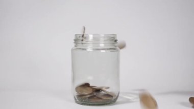 Yavaş paraların cam kavanoza düşmesi birikimleri, banka mevduatlarını, finansal büyümeyi ve para yönetimini sembolize eder..