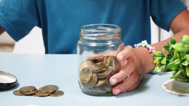 Çocuk cam kavanoza bozuk para koyarak para biriktiriyor, bütçe, mali disiplin ve gelecek planlamasını temsil ediyor.