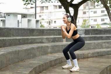 Genç Asyalı bir kadın parkta kulaklık takıyor, spor yapıyor, dışarıda egzersiz yapıyor, sağlık, esneklik, canlılık ve doğada dengeli ve sağlıklı bir yaşam tarzını teşvik ediyor...
