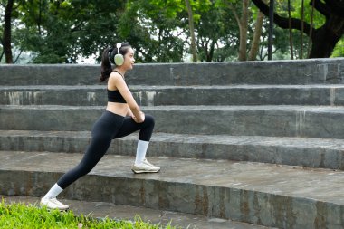 Genç bir kadın bacaklarını açıyor ve parkta kulaklıkla müzik dinliyor..