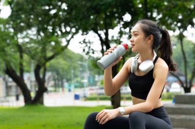 Koştuktan sonra su içen genç bir kadın. Güneşli bir günde açık havada su içen sportif bir kadın...