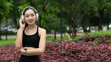 Spor kıyafetli genç Asyalı kadın çiçek parkında kulaklık takıyor, müzik dinlerken doğanın tadını çıkarıyor..