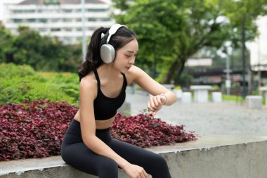 Kulaklıklı spor elbiseli kadın şehir köprüsünde egzersiz yaptıktan sonra nabzını ve saatini kontrol ediyor...