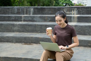 Şehir caddesinde merdivenlerde otururken dizüstü bilgisayar kullanan ve kahve içen serbest çalışan kadın portresi. Blogger konsepti..