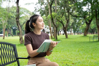 Park defterine yazan kadın. Odaklanmış genç profesyonel günlük tutma, çalışma ya da güneşli bir açık hava bankına not alma. Üretkenlik, eğitim ve refah için ideal..