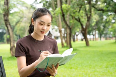 Park defterine yazan kadın. Odaklanmış genç profesyonel günlük tutma, çalışma ya da güneşli bir açık hava bankına not alma. Üretkenlik, eğitim ve refah için ideal..
