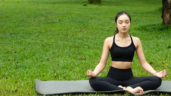 Bir kadın parkta mindere oturmuş, yoga yapıyor. Sahne huzurlu ve sakin. Kadın nefesine ve çevresine odaklanmış durumda..