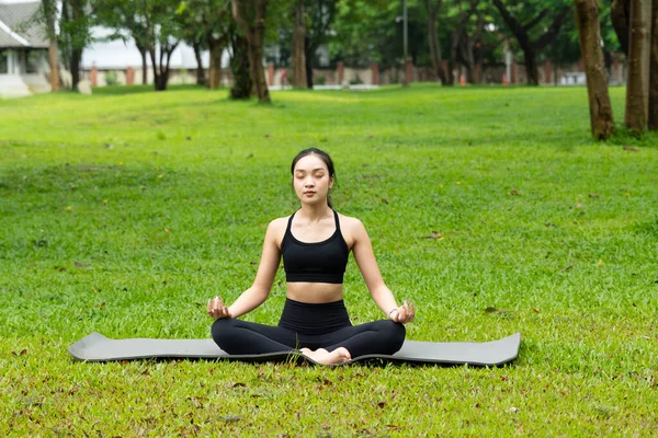 Bir kadın parkta mindere oturmuş, yoga yapıyor. Sahne huzurlu ve sakin. Kadın nefesine ve çevresine odaklanmış durumda.