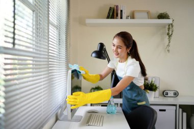 Ofisteki ıslak temizlik sırasında bilgisayar ekranını silmek için deterjan kullanan sarı eldivenli bir işçi..