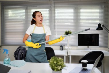 Bir ofis odasını temizlerken yeşil önlüklü bir kadın şarkı söylüyor. Elinde bir paspas var ve yaptığım işten memnun..