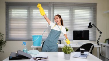 Bir ofis odasını temizlerken yeşil önlüklü bir kadın şarkı söylüyor. Elinde bir paspas var ve yaptığım işten memnun...