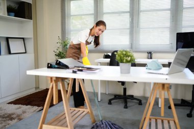 Temizlik işçisi yerleri paspasla yıkıyor, yakın plan. Ofiste içi malzeme dolu bir kova..