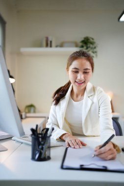 Takım elbiseli bir kadının parlak bir ofis yerinde masa üzerinde kalemle bir belgeyi imzalarken..