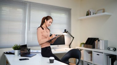 Bir kadın elinde bilgisayar monitörü ve bir panoyla masanın önünde duruyor..