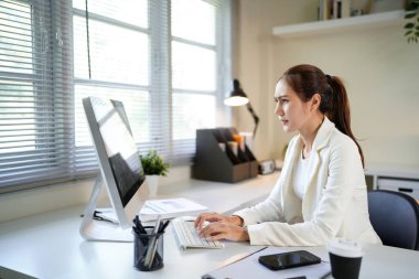 Önünde bilgisayar monitörü olan bir kadın büro masasında oturuyor. Suratı asık bir şekilde ekrana bakıyor..