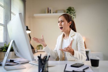 Önünde bilgisayar monitörü olan bir kadın büro masasında oturuyor. Suratı asık bir şekilde ekrana bakıyor..