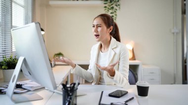 Önünde bilgisayar monitörü olan bir kadın büro masasında oturuyor. Suratı asık bir şekilde ekrana bakıyor..