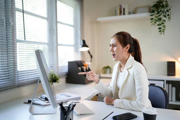 Önünde bilgisayar monitörü olan bir kadın büro masasında oturuyor. Suratı asık bir şekilde ekrana bakıyor..