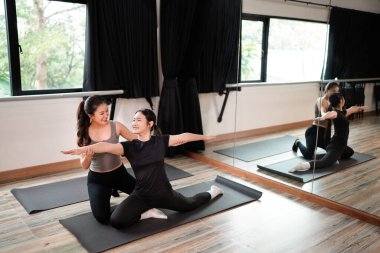 İki kadın spor salonundalar, biri yoga yapıyor, diğeri de onu izliyor..