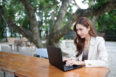 Evde çalışan serbest çalışan Asyalı bir kadın, iş kadını sabah bahçede masada oturan bir dizüstü bilgisayarla çalışıyor. Ev konseptinde çalışan yaşam tarzı kadınları..