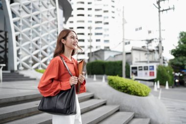 Güzel bir Asyalı iş kadını klasörler taşıyor ve şirket binasının dışında duruyor...