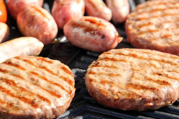 Shallow focus shot of tasty assorted delicious sausages and burgers sizzling and cooking on a barbecue griddle plate, outside in bright summer sunshine