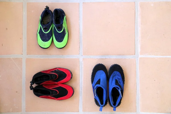 Üç çift resif ayakkabısı, ya da su ayakkabısı, yeşil, kırmızı ve mavi renkte, terasotta döşemeli zeminde bir desen oluşturuyor.