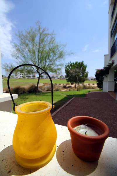 Küçük sarı ve terracotta tencereleri, taştan bir çıkıntıda, parlak bir arka planda golf sahası ve daireleri var.