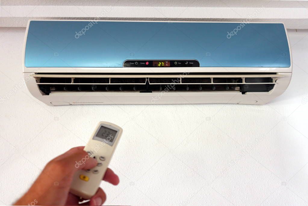 Someone changing the settings of a domestic AC or Air Conditioning unit with a remote control - focus on the wall unit - copy space for text