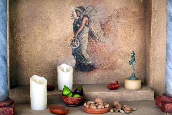 Cartagena, Murcia, İspanya - 01 Ağustos 2018: Bir meleğin resmedildiği küçük bir duvar resminin önünde incir, fındık ve mumların sergilenmesi