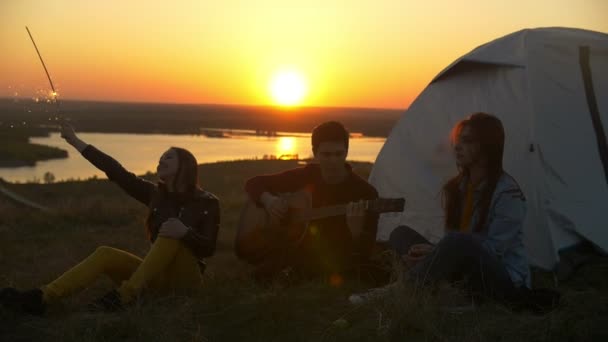 Jóvenes amigos divirtiéndose con bengalas y canciones con guitarra al atardecer al aire libre — Vídeos de Stock