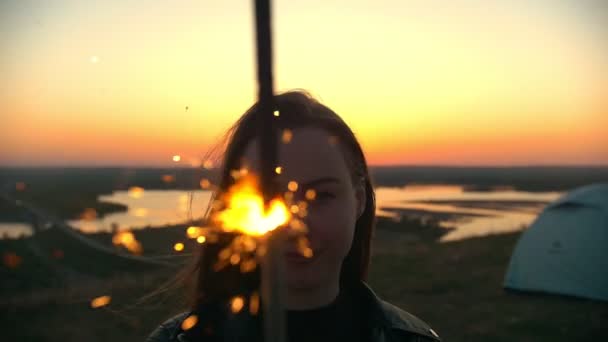 Retrato de mulher jovem com sparkler fica em uma colina no pôr do sol de verão — Vídeo de Stock