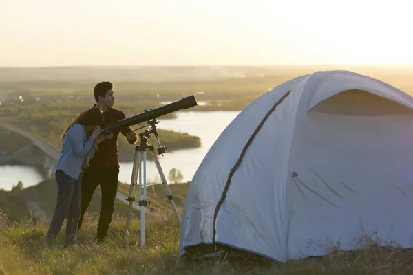 Young friends looking through telescope on the hill at summer ev