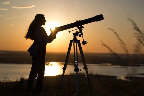 Силует молодої жінки, яка дивиться через телескоп на літній захід сонця — стокове фото
