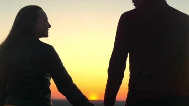 Feliz pareja joven tomados de la mano mirando el uno al otro en el increíble atardecer al aire libre — Vídeo de stock