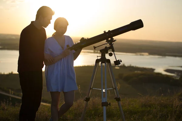 Giovane coppia amorevole guardando attraverso il telescopio sulla collina a — Foto Stock