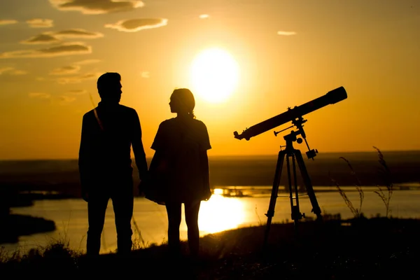 Siluetter av par nära teleskopet på kullen på sommar solnedgång — Stockfoto