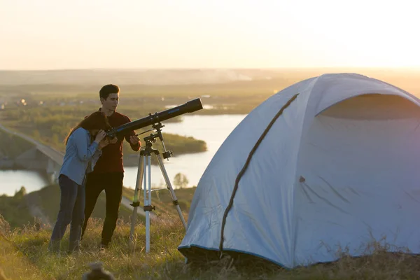 stock image Young friends looking through telescope on the hill at summer ev