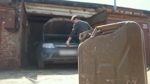 Канистра стоит перед молодым человеком ремонт двигателя автомобиля в гараже — стоковое видео