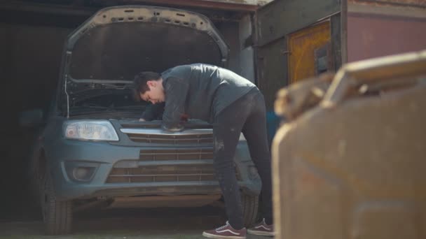Канистра стоит перед молодым человеком ремонт автомобиля в гараже — стоковое видео